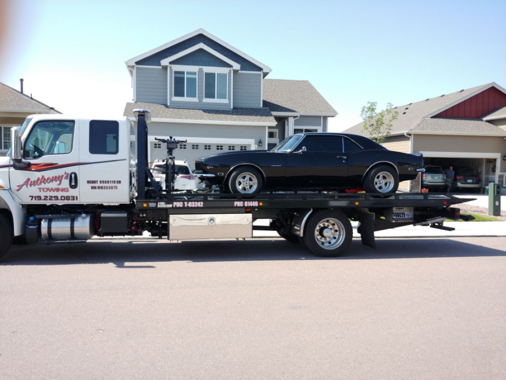  A reliable Anthony's Towing tow truck securely transports a black vehicle from a residential area.