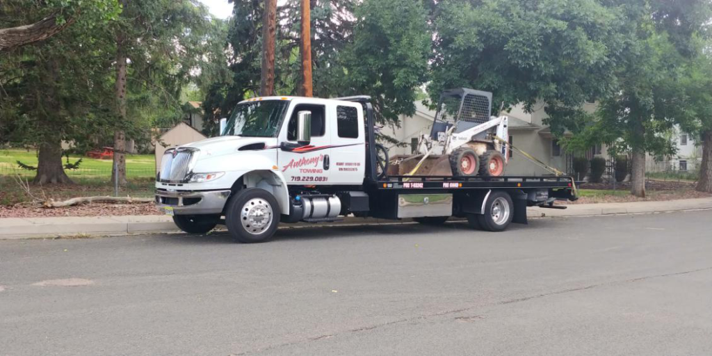 A reliable Anthony's Towing tow truck securely transports a small snow removal vehicle